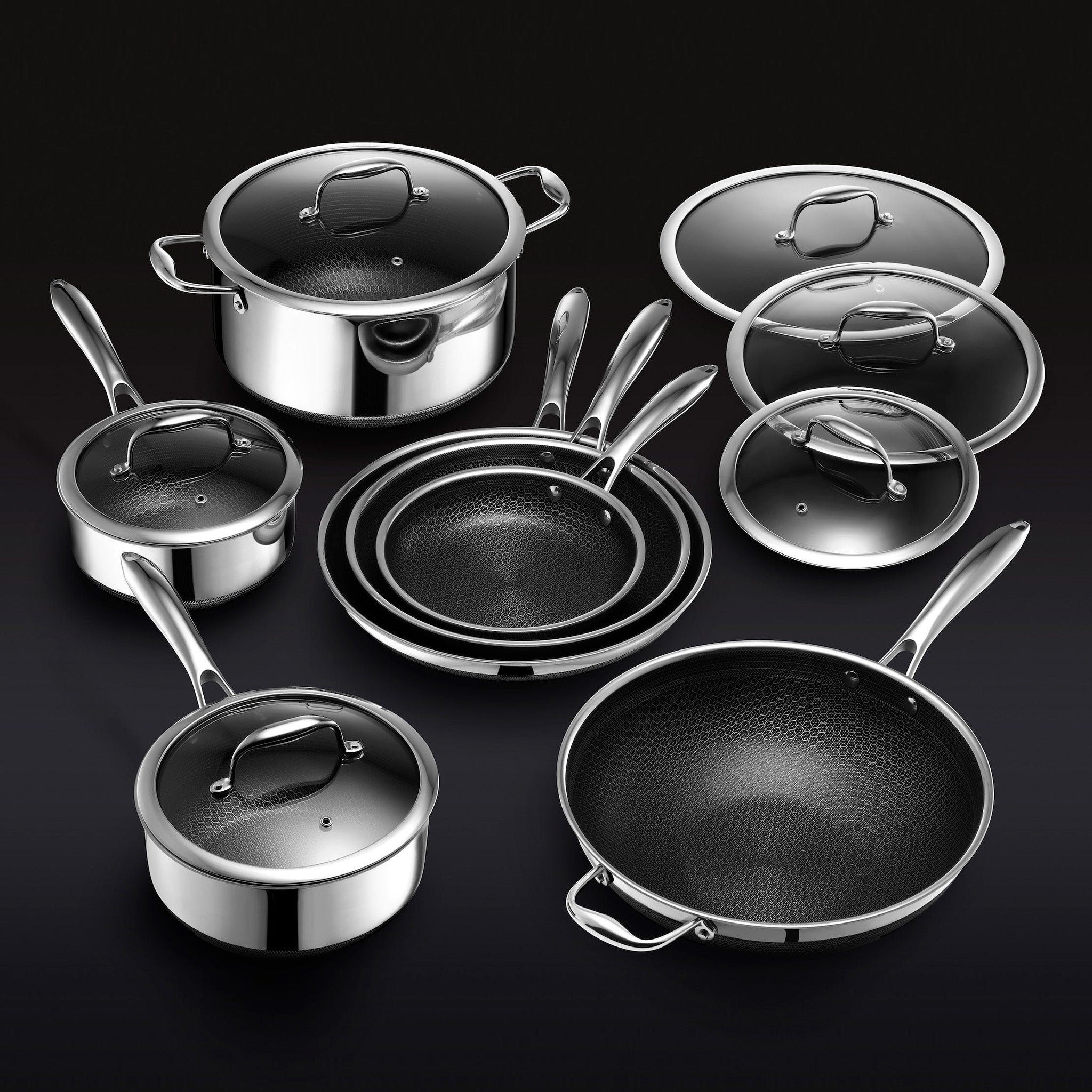 Set of stainless steel pots and pans with lids on a dark background.